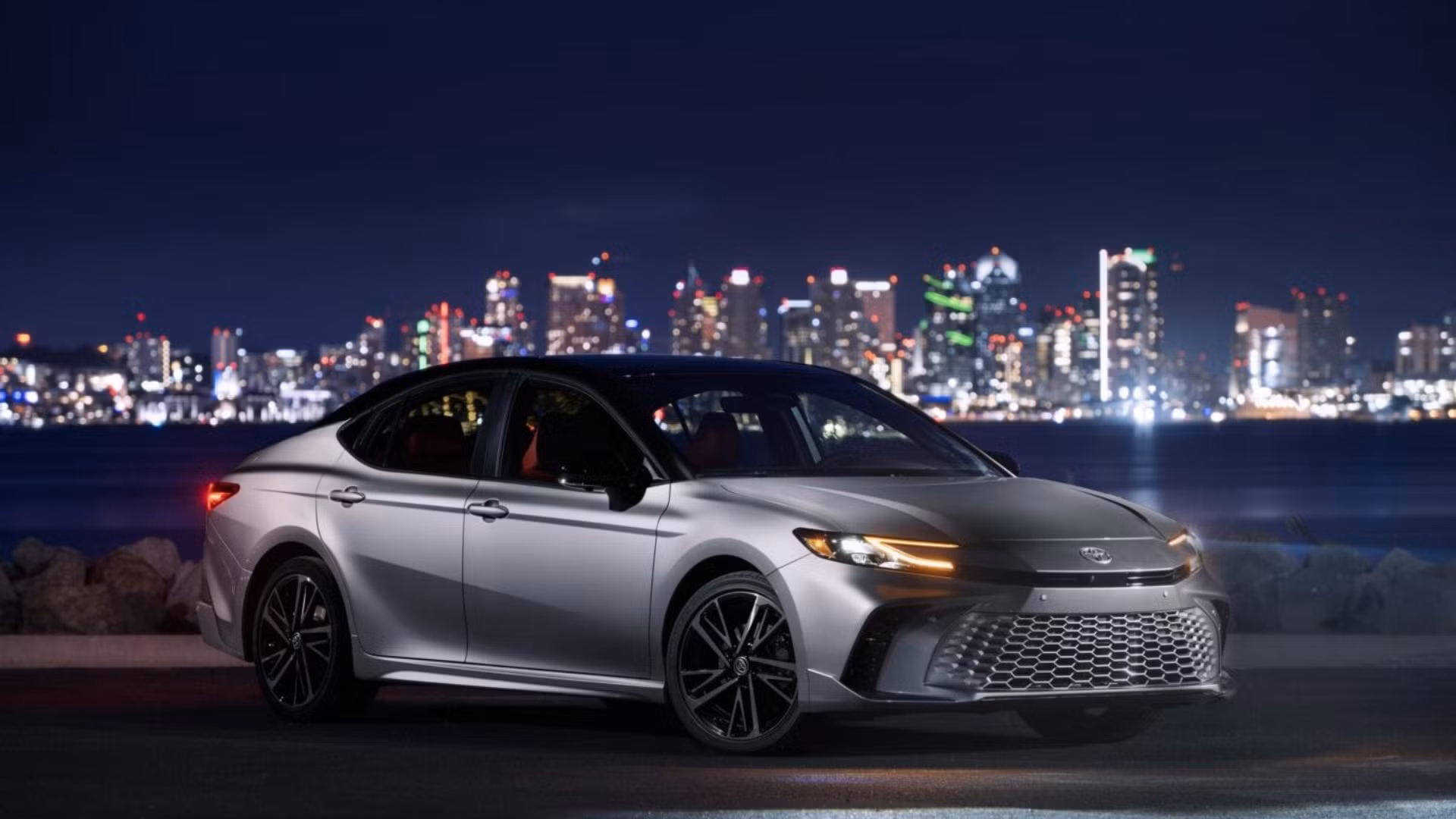 2025 Toyota Camry parked at night with a city skyline in the background