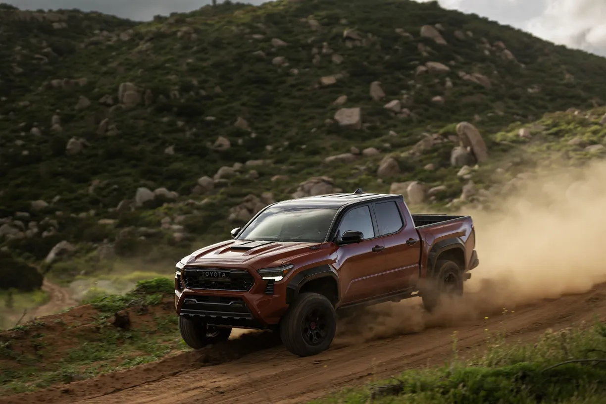 A dark red Toyota Tacoma TRD Off-Road pickup truck kicking up dust while descending a rocky mountain trail