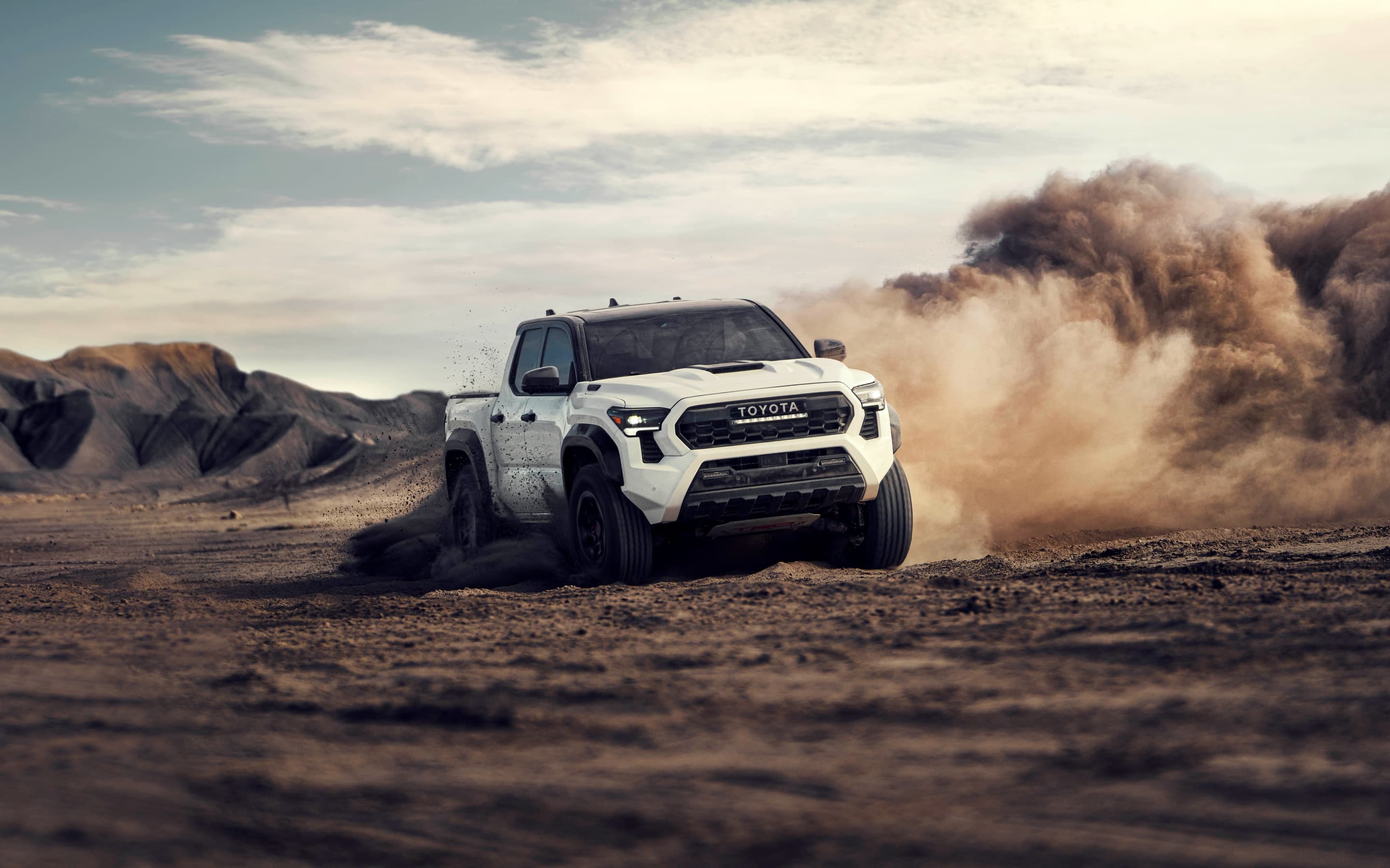 A white Toyota Tacoma TRD Pro pickup truck kicking up a large dust cloud while driving through a desert off-road course